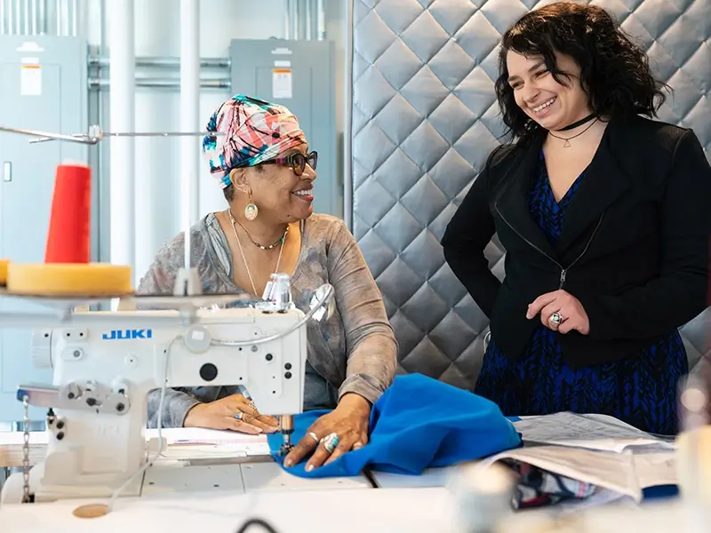 Dos mujeres de pie junto a una máquina JUKI