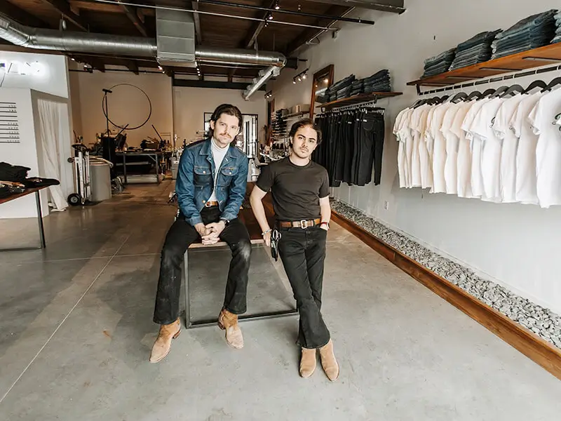 Dois homens olhando para uma câmera, eles estão dentro de uma loja de roupas